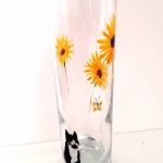 A small vase with a balcka nd white cat watching a butterfly and sunflowers